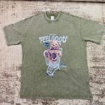 Vintage-wash olive green streetwear t-shirt featuring a graphic of a brown teddy bear in a shopping cart under 'Feel Good' text, custom DTF printed by Whavieprints.